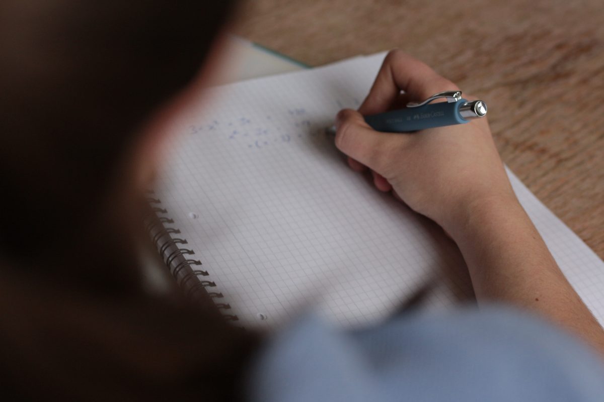 A woman holding a pen while writing formulas on graph paper in a notebook.