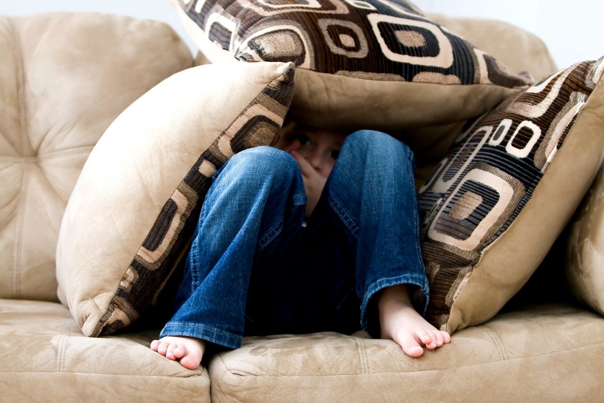 Photo of a child hiding underneath pillows on a couch.