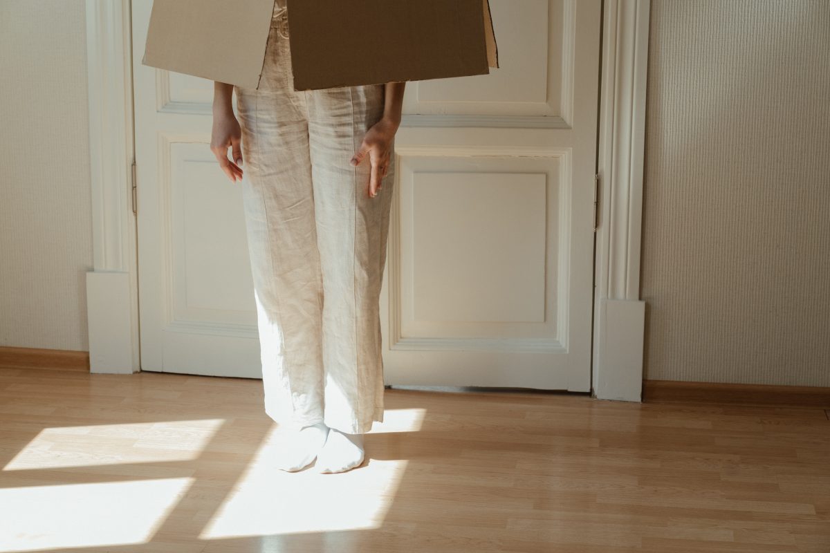 A light-skinned person stands in a room with a box over their head.